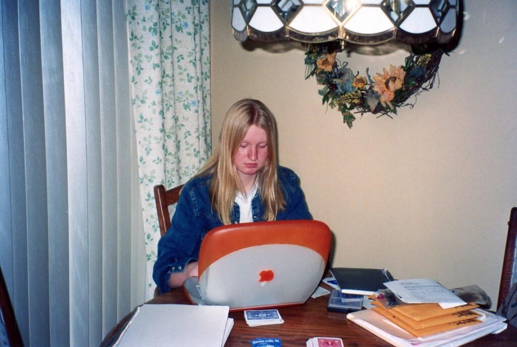 Ashley as a teen typing on an orange clamshell Apple iBook