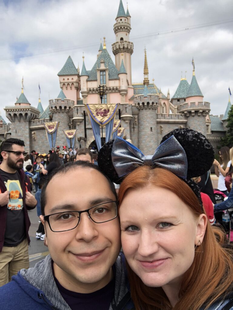 Photo of Ashley (in Minnie Mouse ears) and her husband with the Disney castle in the background, Disneyland